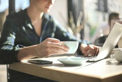 Mann trinkt einen Kaffee und schaut dabei auf sein Laptop.