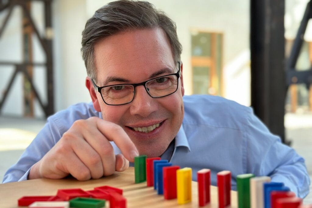 Symbolbild SPIN Selling Training: Oliver Schumacher stößt ein Domino-Spielfeld an.