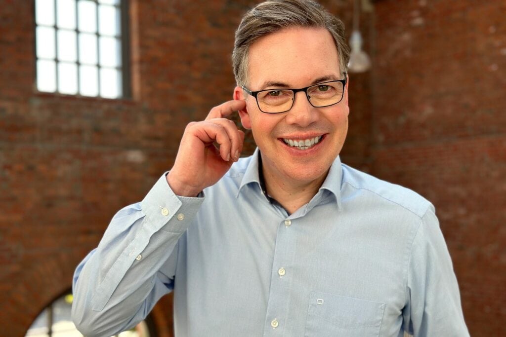 Symbolbild Mindest im Vertrieb: Oliver Schumacher kratzt sich am Ohr.