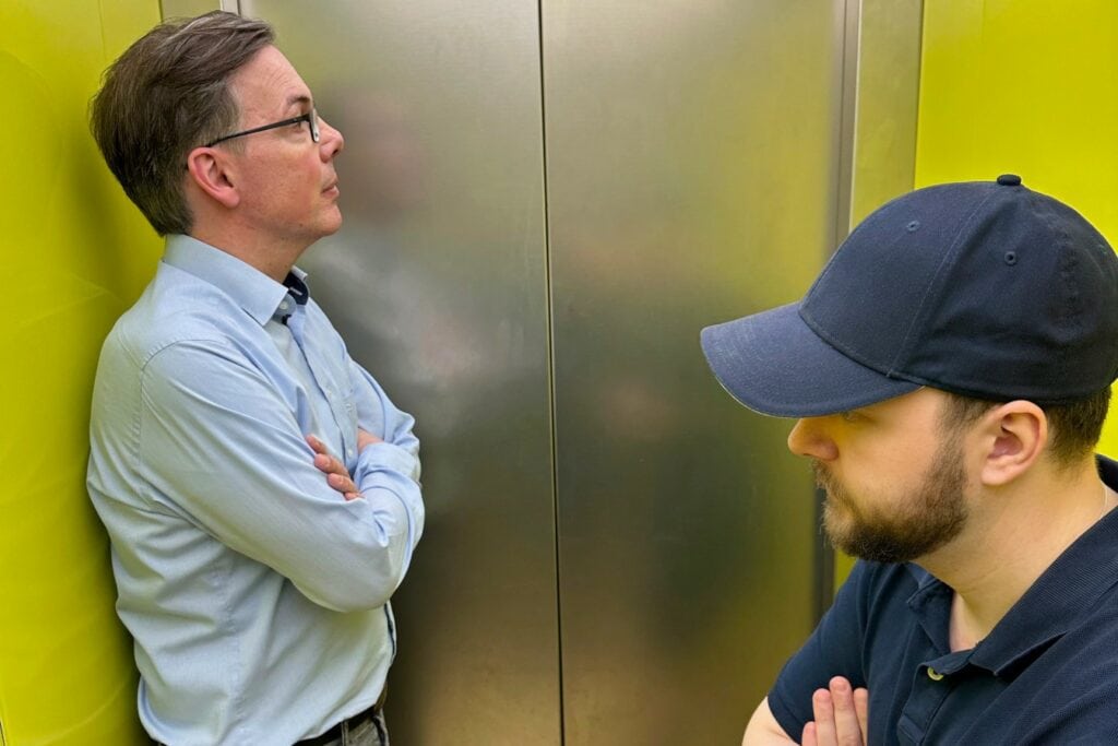 Symbolbild Gesprächsaufhänger bzw. Gesprächseinstieg: Oliver Schumacher und weiterer Fahrgast schweigen sich im Fahrstuhl an.