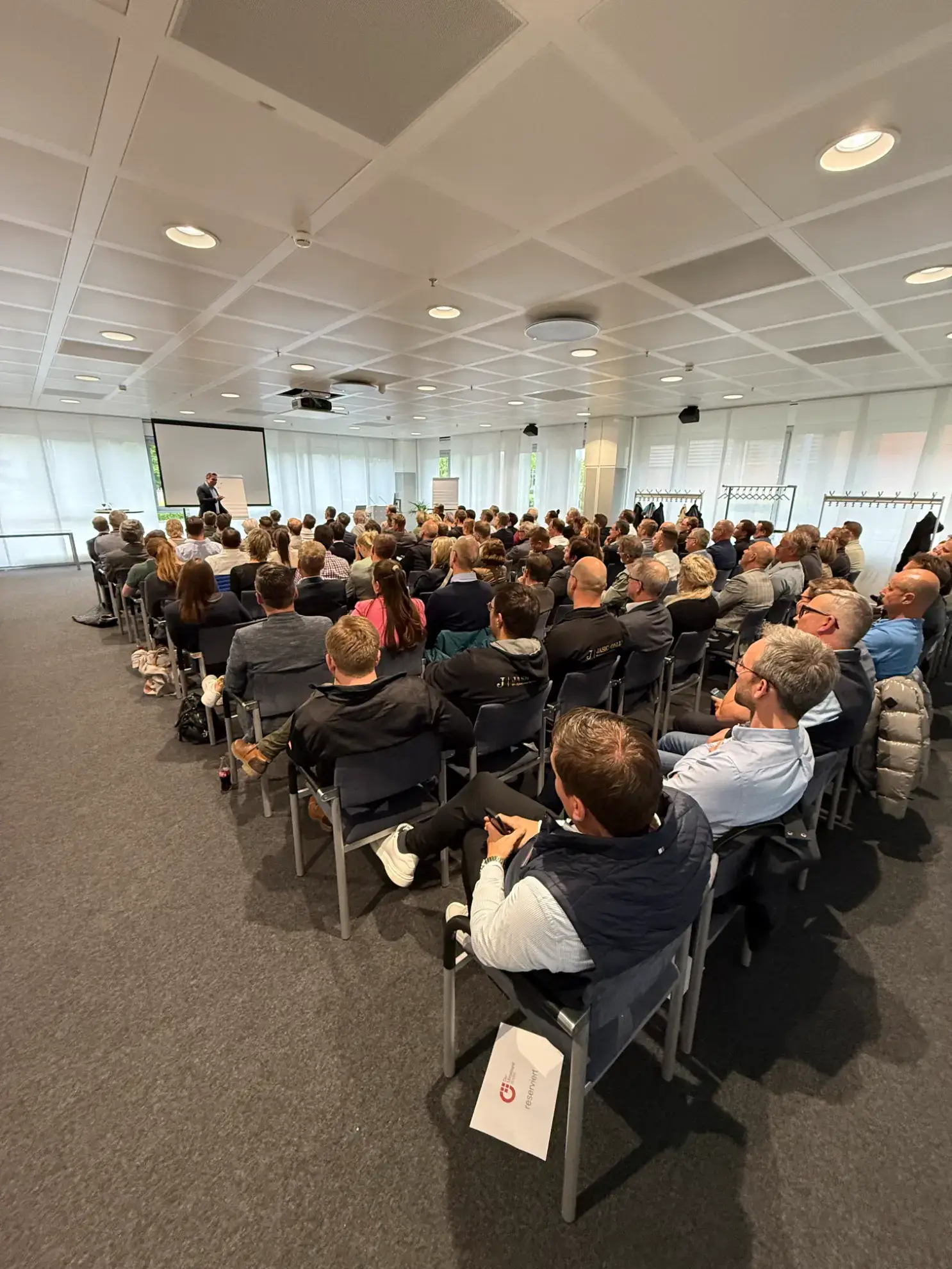Eine große Gruppe von Menschen sitzt in einem modernen Konferenzraum und hört einem Verkaufstrainer während eines ansprechenden Verkaufstrainings zu.