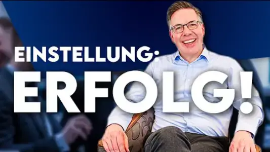 Ein lächelnder Oliver Schumacher mit Brille sitzt auf einem Stuhl; deutscher Text: Einstellung: Erfolg! (Einstellung: Erfolg!). Ideal für jeden Verkaufstrainer, der nach Inspiration sucht.